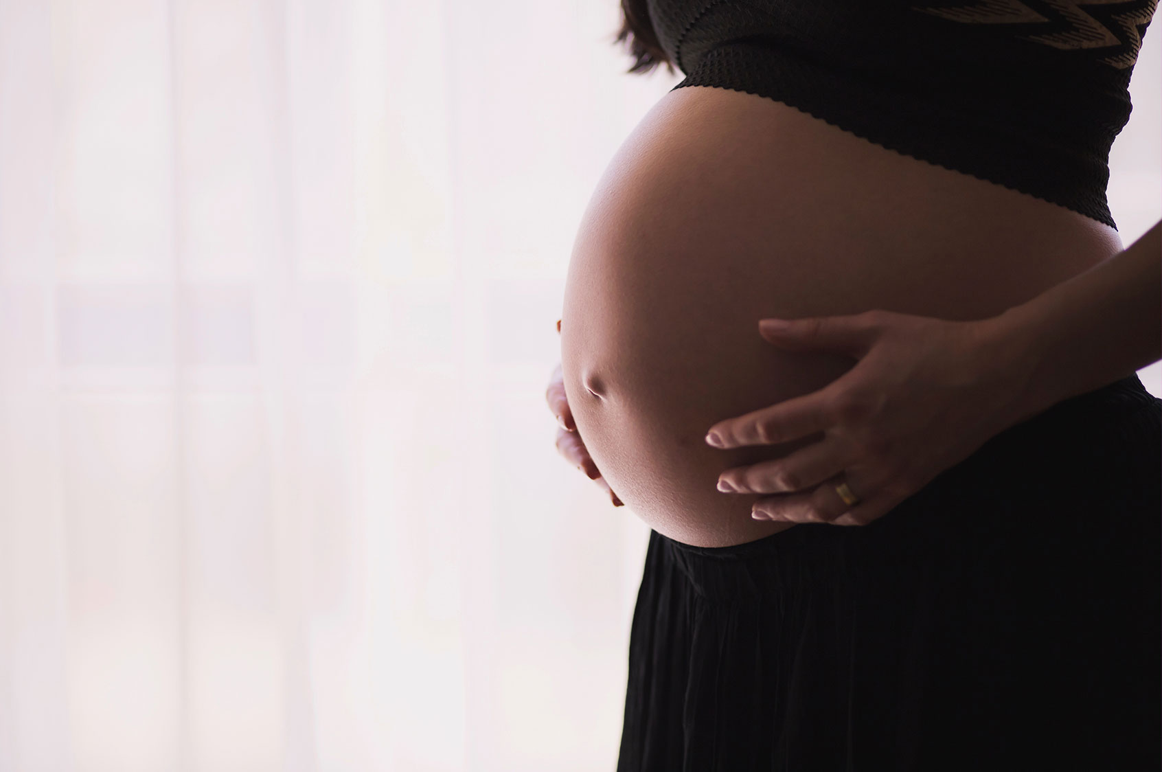 Expectant mother cradling her pregnant belly in front of a sunlit window