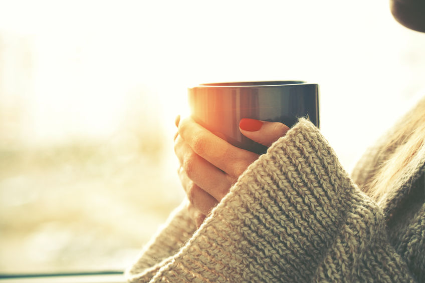 Hands in a knit sweater cradling a warm mug of tea by a sunlit window
