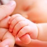 Newborn baby's hand gripping an adult's finger