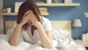 Woman sitting on a bed with her face in her hands during endometriosis pain
