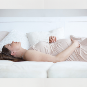Pregnant woman resting on a bed with one hand on her belly