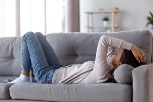 Woman lying on a couch with a hand pressed to her head during a migraine
