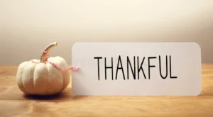White pumpkin beside a card reading Thankful on a wooden table