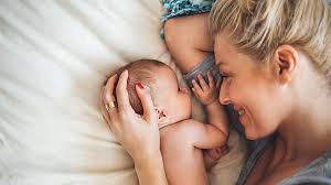 Mother lying beside her newborn baby, smiling, during the postpartum period